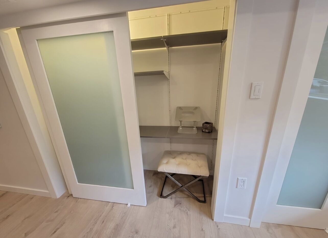 Un dressing accessible sans porte, doté d’une tringle à vêtements avec un miroir, d’un petit tabouret et d’un interrupteur sur le mur.