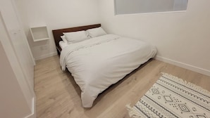 Ein Schlafzimmer mit einem Bett, einem Fenster, einer kleinen Ablage und einem Teppich mit Muster.