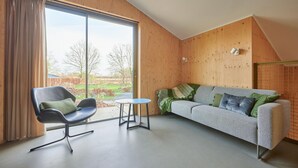 Een moderne woonkamer met een grote schuifpui, een zwarte stoel, een klein rond tafeltje en een grijze bank met gekleurde kussens.