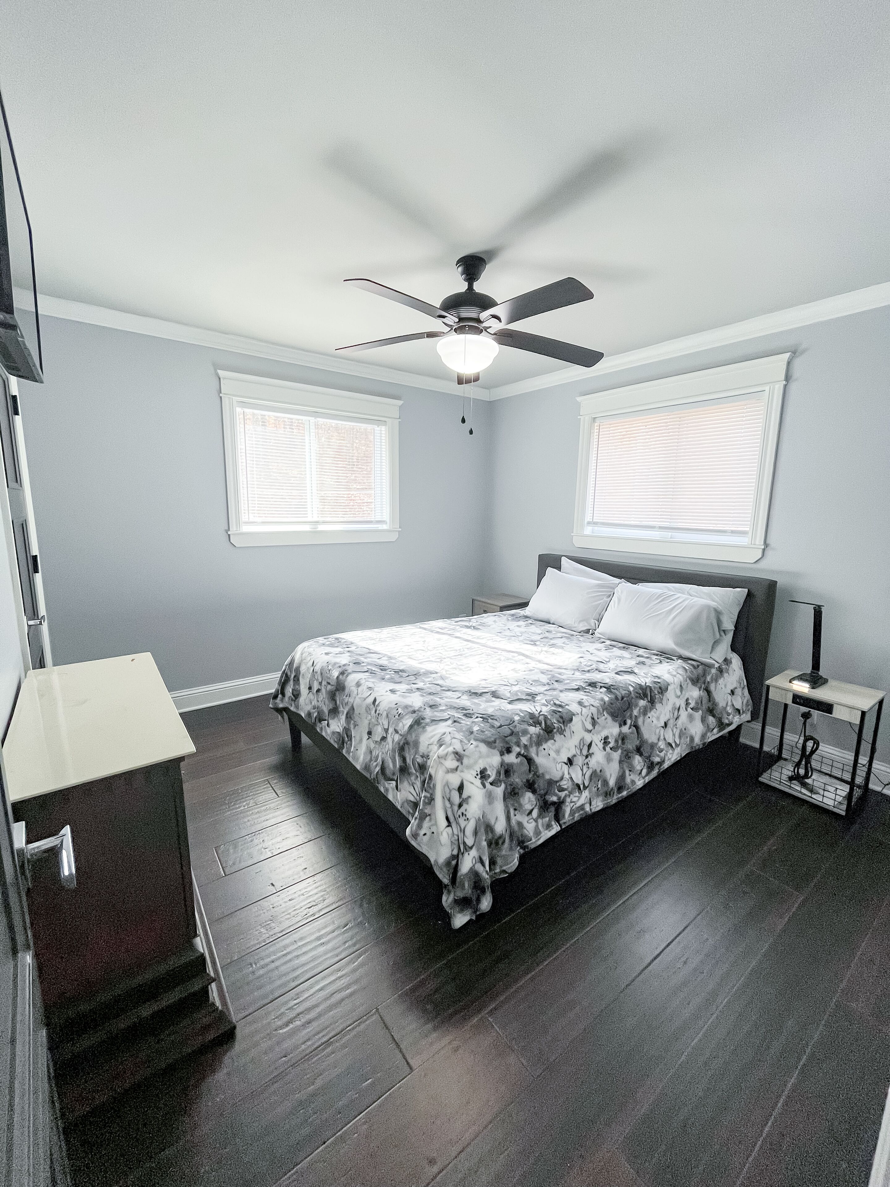 A bedroom with a bed, a ceiling fan, a nightstand, and a dresser.