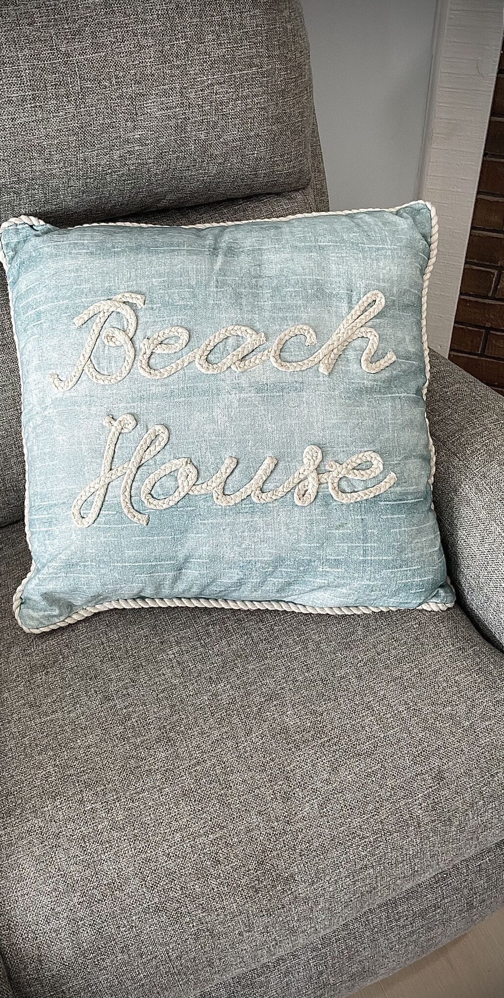 Almofada azul clara com a inscrição 'Beach House' bordada numa fonte cursiva.
