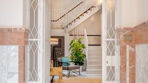 Una escalera que lleva a un piso superior, un área de descanso con una silla y una mesa, y una planta en maceta.