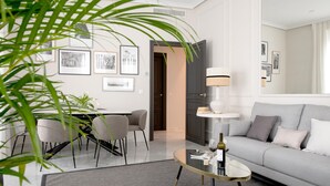 Una sala de estar moderna con un sofá gris, una mesa de centro de vidrio y cuadros enmarcados en la pared.