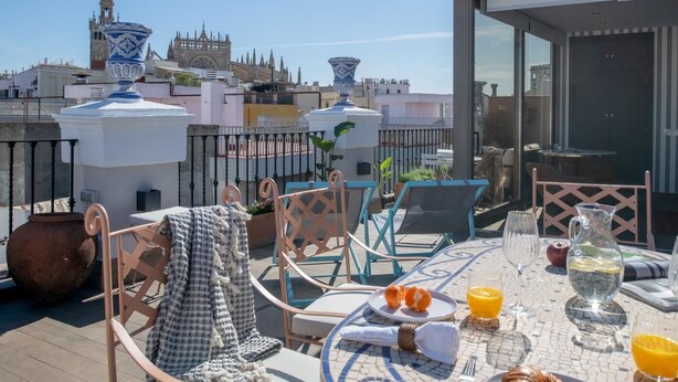 Terraza en la azotea con una mesa dispuesta para el desayuno, con vistas a un paisaje urbano histórico de arquitectura singular.