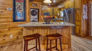 Eine gemütliche Küchenzeile in einer Holzhütte mit Holzwänden, einer Granitabdeckung, einem Kühlschrank, einer Mikrowelle, einem Spülbecken und einer Waschmaschine.