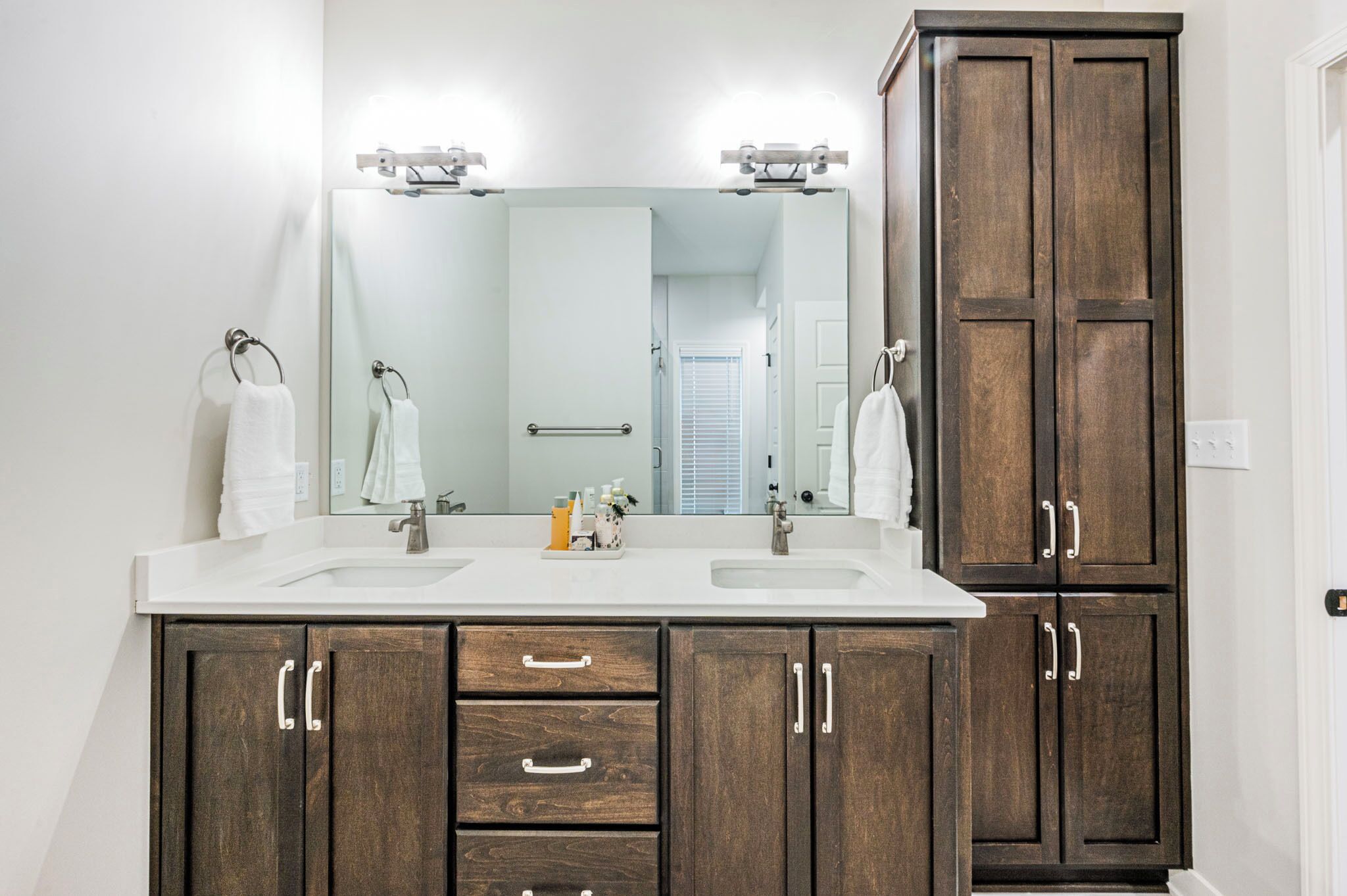 A bathroom with a double sink, wooden cabinets, a large mirror, and a towel rack.