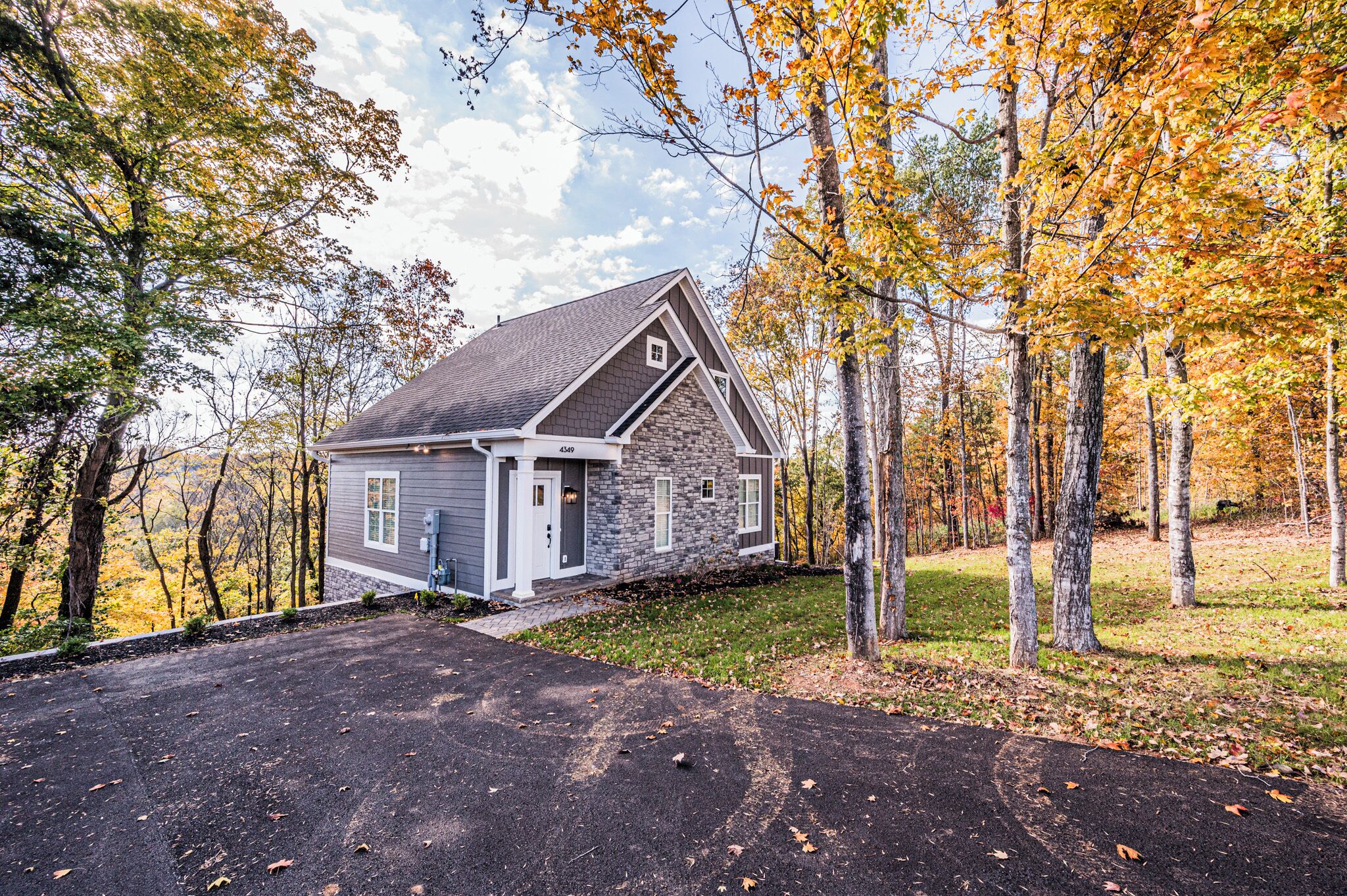 A two-story house with a stone exterior, a grey roof, and a driveway leading to the entrance.