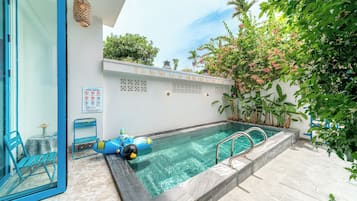 A swimming pool with a clear blue water, surrounded by a white wall with a sign, a blue chair, and a blue inflatable float.
