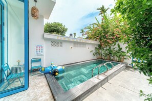 A swimming pool with a clear blue water, surrounded by a white wall with a sign, a blue chair, and a blue inflatable float. - Hoi An Lazy Bear Hostel (Da Nang)