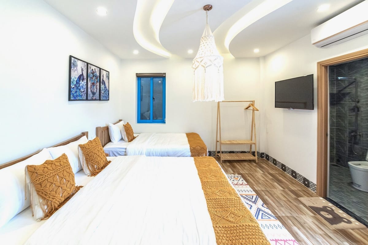 A hotel room with two beds, a hanging light fixture, a TV, and a blue door.
