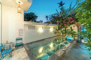 A swimming pool area with a lounge chair, a table with a vase, and a sign with pool rules. - Hoi An Lazy Bear Hostel (Da Nang)