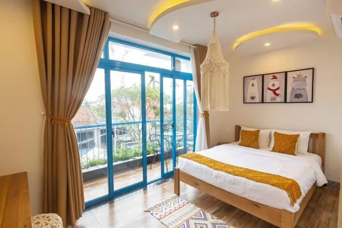 A bedroom with a large window, a bed with white bedding, a hanging light fixture, and a view of the outdoors.