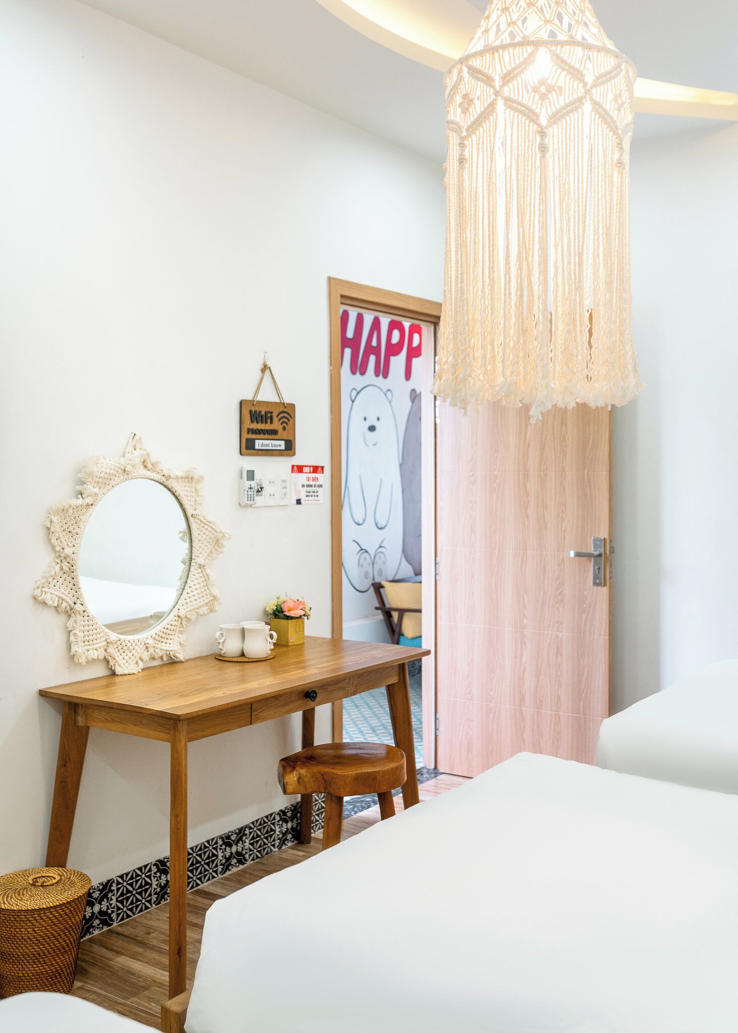 Un dormitorio con un escritorio de madera, un espejo de macramé, una lámpara colgante y una puerta con un letrero que dice 'HAPP'.