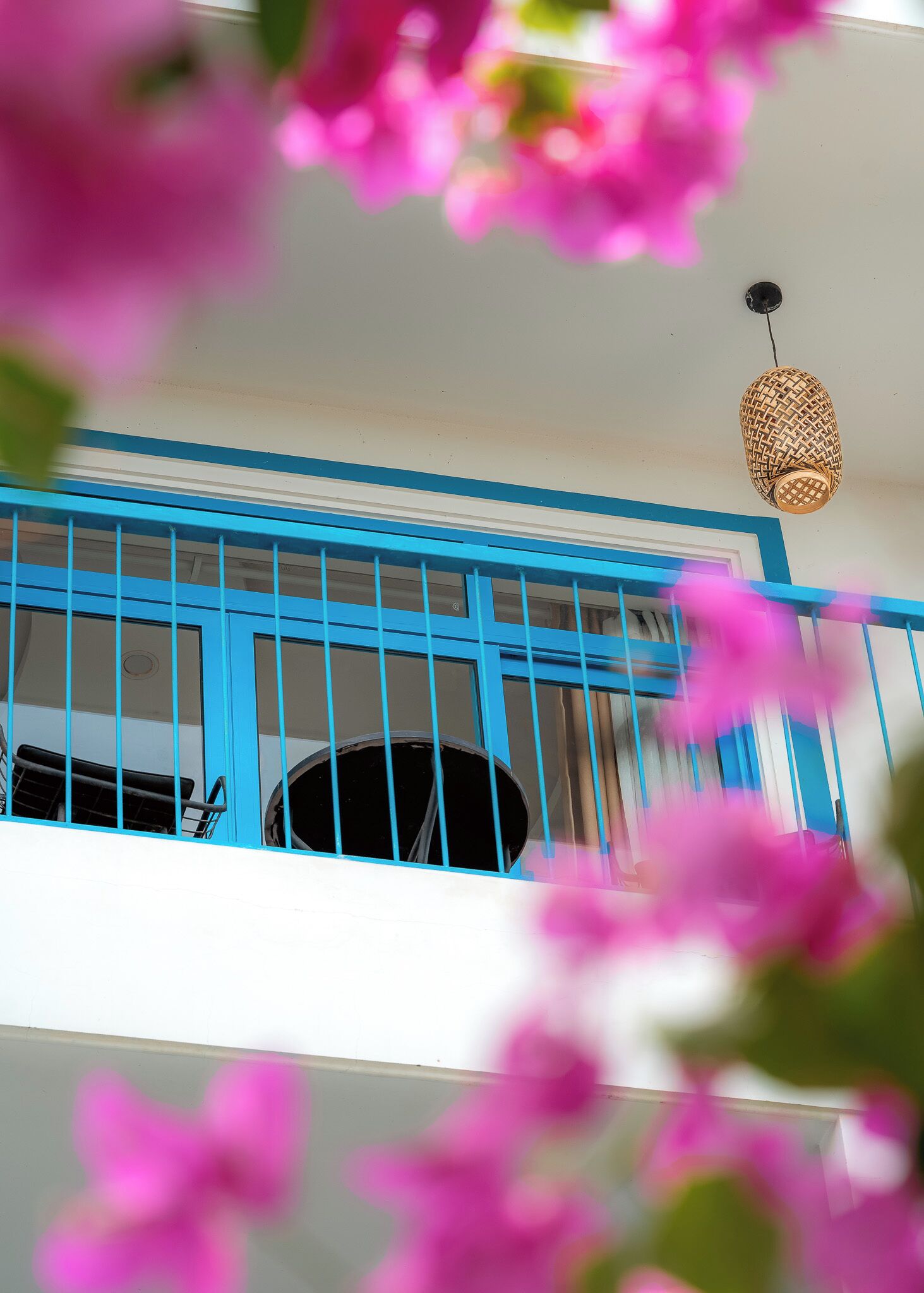 Una habitación con barandilla azul, lámpara colgante y ventana con cortinas.