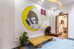 A room with a wall mural of a bear and a panda on a crescent moon, a wooden bench, and a potted plant.