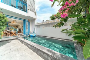 Piscina con superficie de agua azul clara, rodeada por un muro blanco con plantas decorativas y un cartel.