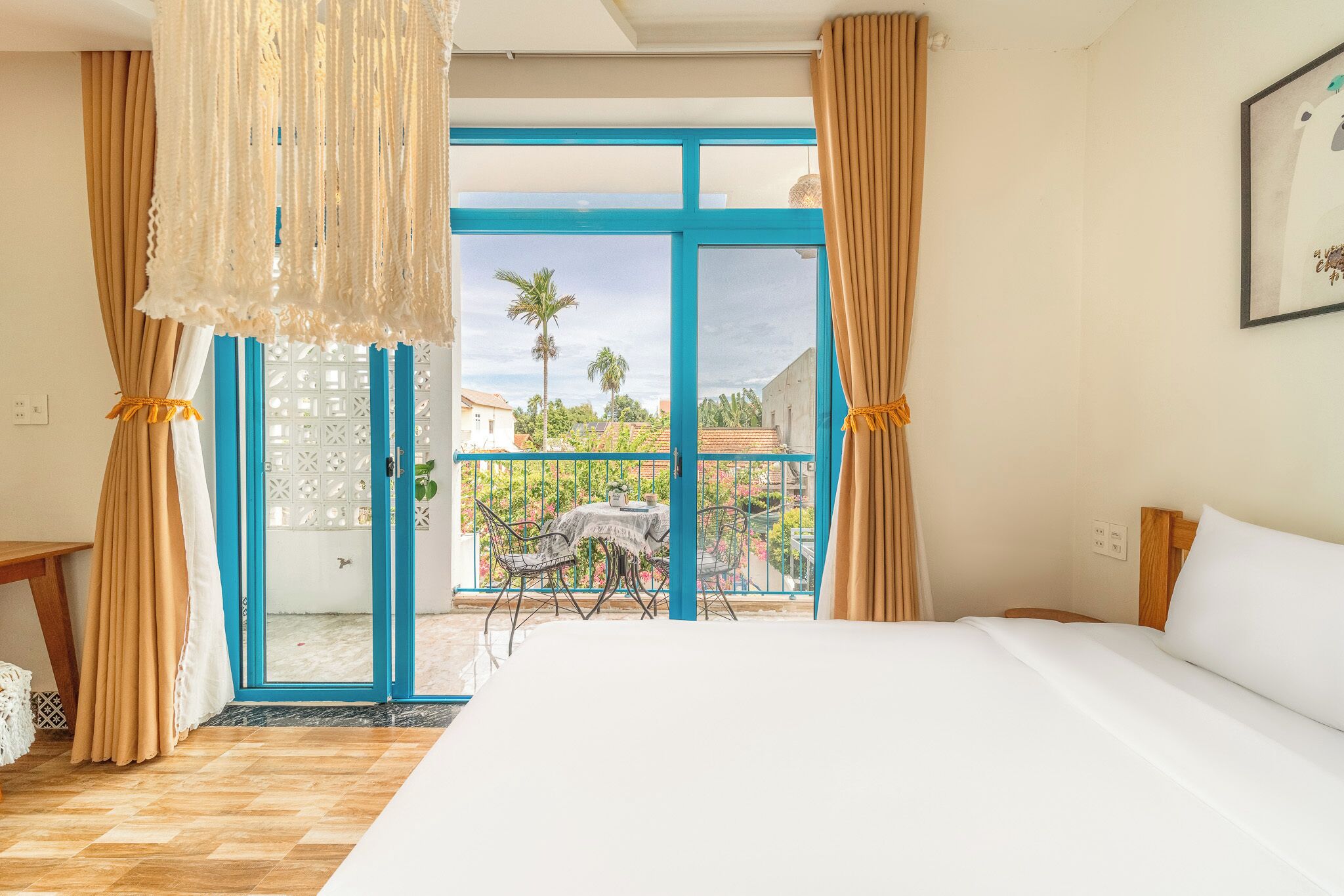 A hotel room with a large bed, a balcony with a view of the surrounding area, and a table with chairs outside.