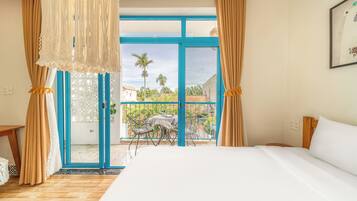 A hotel room with a large bed, a balcony with a view of the surrounding area, and a table with chairs outside.