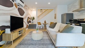 A modern living room with a flat-screen TV, a round coffee table, a patterned rug, and a white sofa. - Charming Guest House - Dog Friendly - Parking (Wilmington)