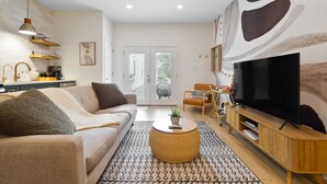 A modern living room with a sofa, coffee table, TV, and kitchen area. - Charming Guest House - Dog Friendly - Parking (Wilmington)