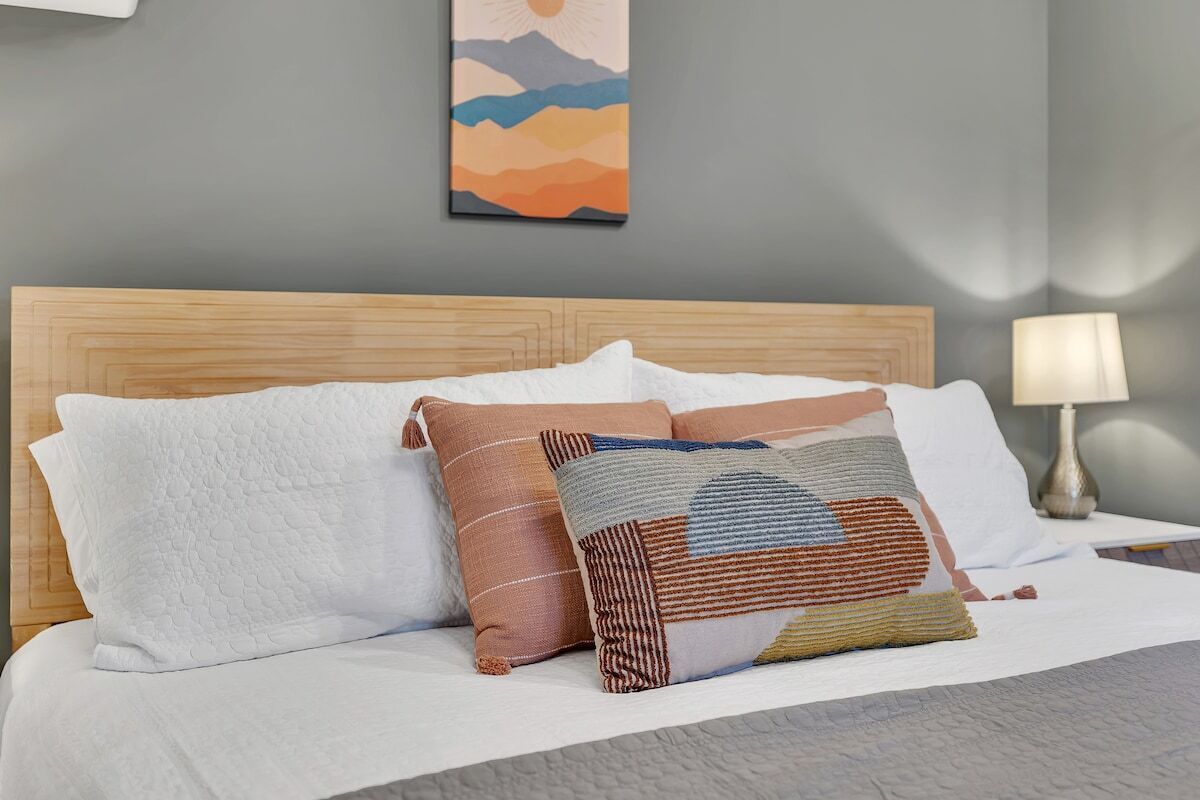 Un lit bien fait, avec une tête de lit en bois, une literie blanche et une variété d’oreillers à motifs.