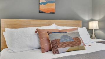 Un lit bien fait, avec une tête de lit en bois, une literie blanche et une variété d’oreillers à motifs.