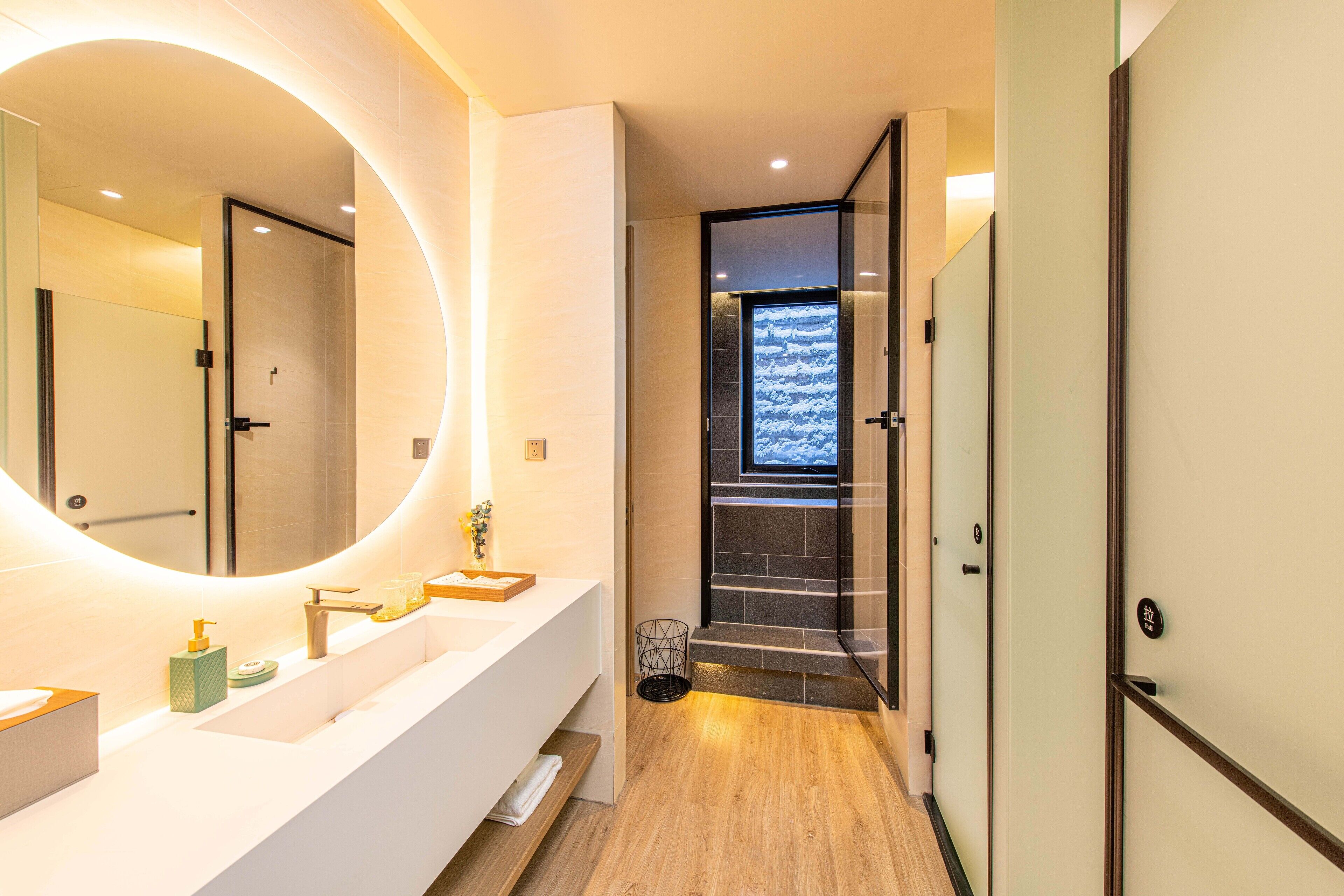 A modern bathroom with a large mirror, a white vanity, and a wooden floor.