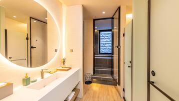 A modern bathroom with a large mirror, a white vanity, and a wooden floor.
