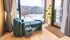 Una sala de estar moderna con un sofá, una mesita con objetos decorativos, vistas a montañas nevadas y una planta en maceta.