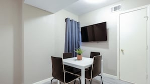 A small, clean room with a white table, four chairs, a potted plant, a flat-screen TV, and a door.