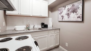 A kitchen with white cabinets, a granite countertop, a stove, and a coffee maker.
