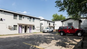 A parking lot with a white building, a red vehicle, and a white vehicle parked.