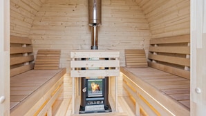 A wooden sauna with benches and a central fireplace.