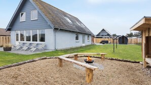 A two-story house with a sloped roof, a patio with a fire pit, and a wooden deck.