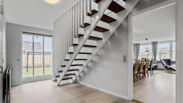 A modern interior with a wooden staircase, large windows, and a dining area.