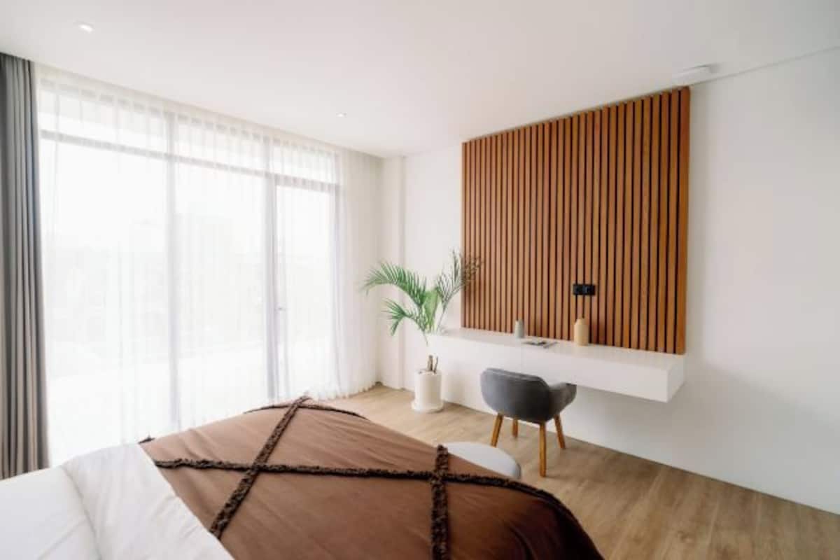 Une chambre moderne avec un grand lit, un bureau, une chaise et une plante en pot.