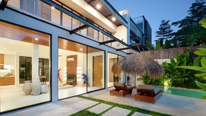 A modern house with large glass windows, a swimming pool, and a thatched umbrella. - Paradise Living Villa Canggu (Canggu)