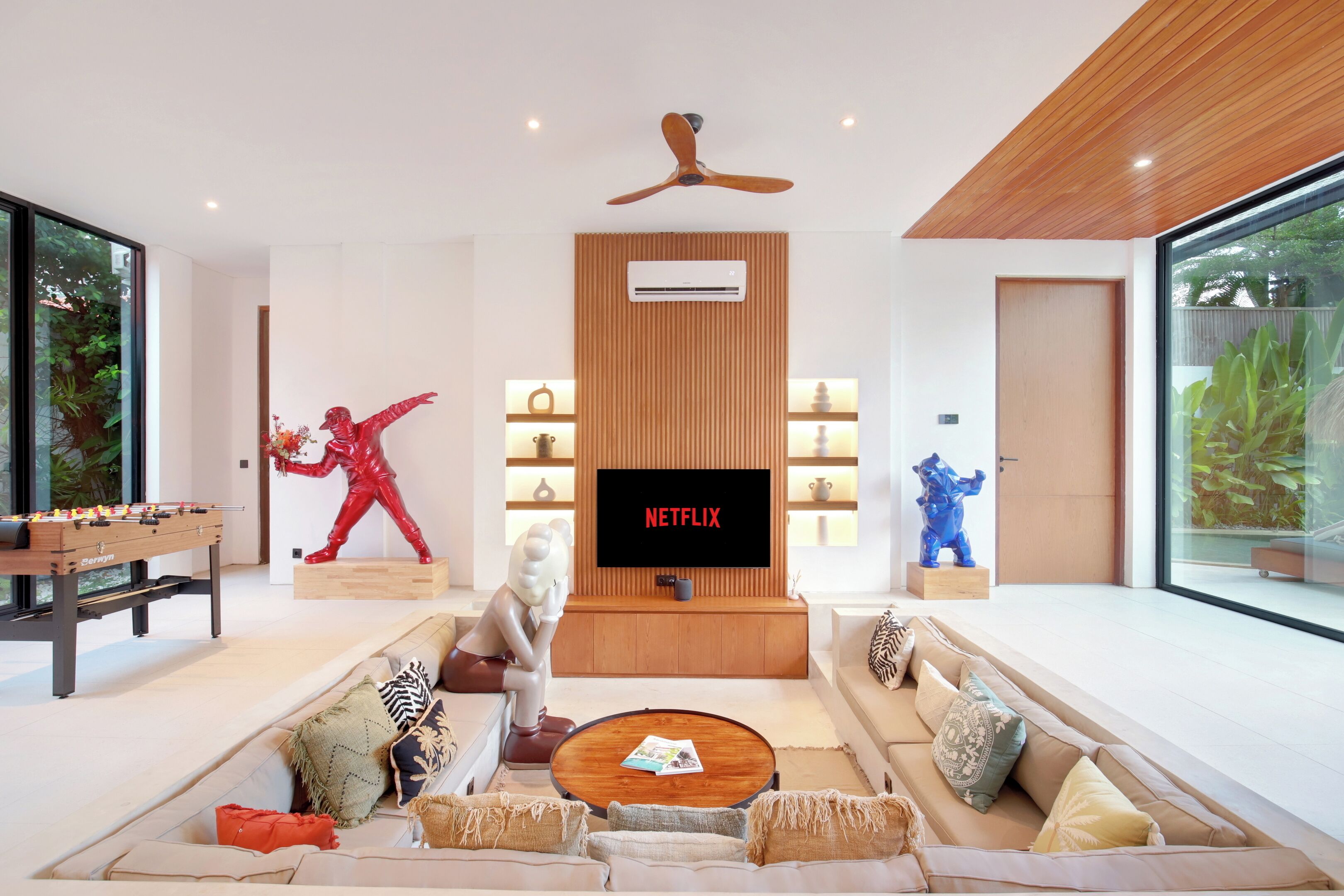 A modern living room with a foosball table, a large flat-screen TV, and a ceiling fan.