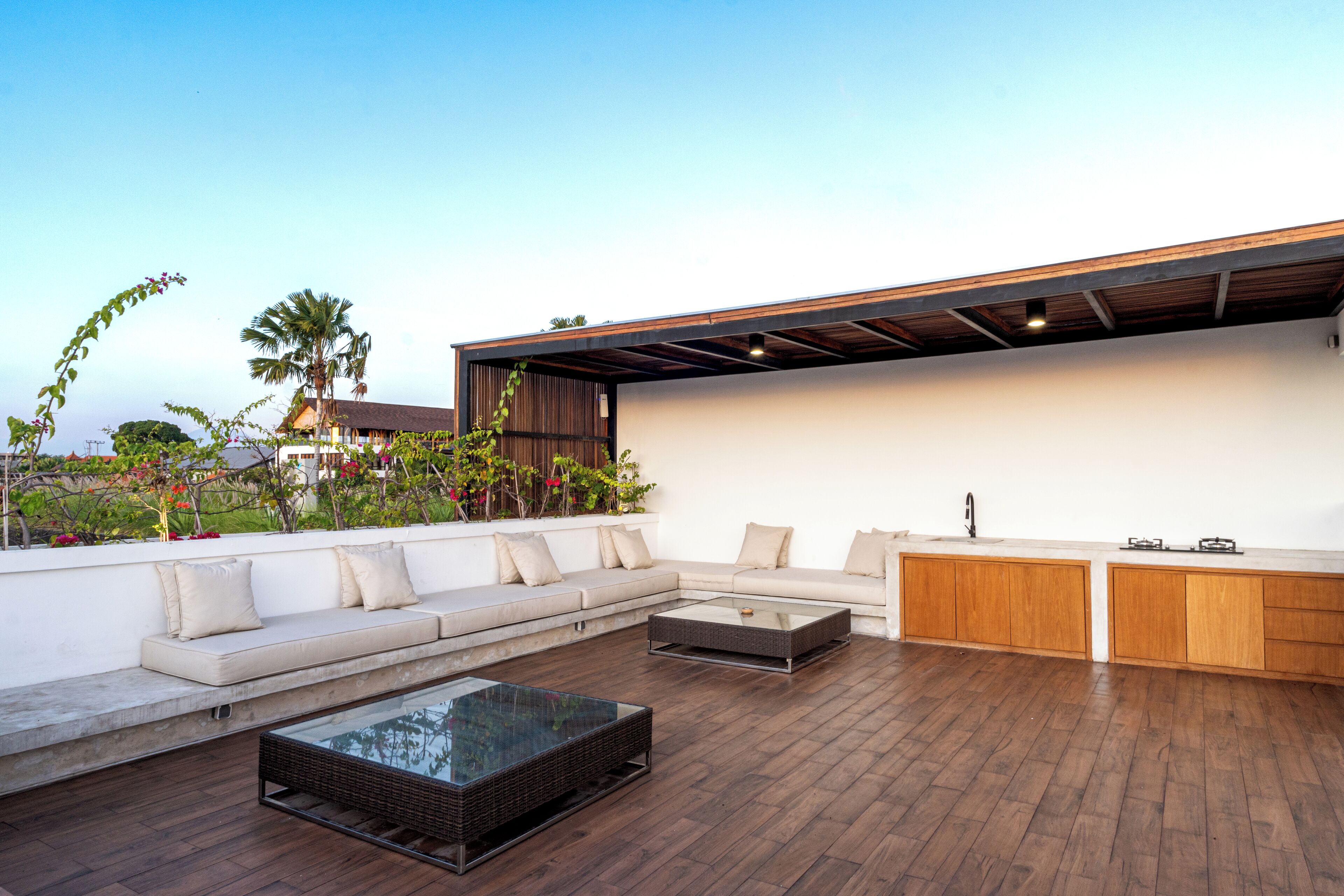 A rooftop patio with a sofa, a glass-top coffee table, wooden cabinets, and a view of the city skyline.