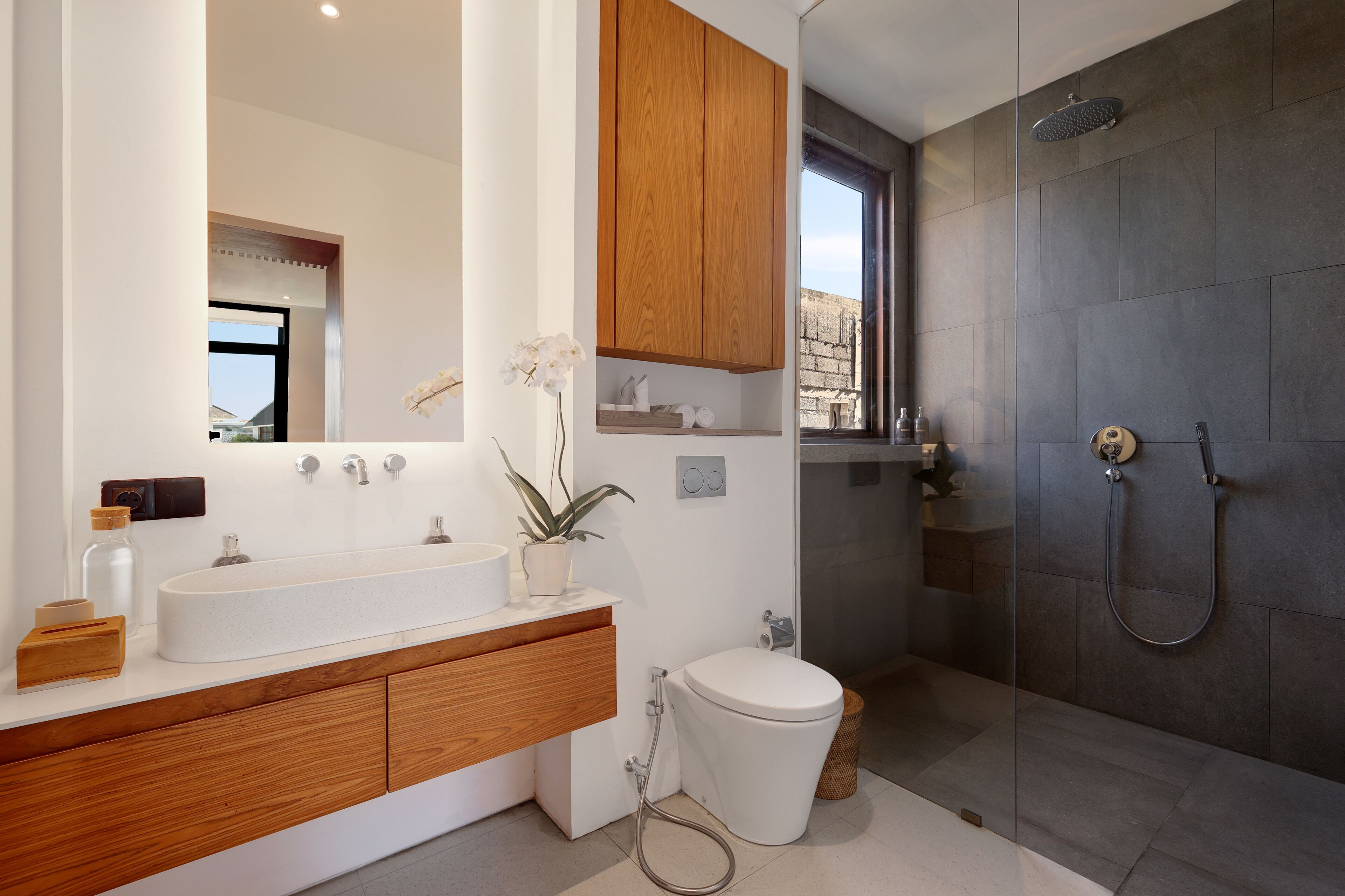 Une salle de bain moderne avec un meuble-lavabo en bois, un lavabo blanc, des toilettes et une douche à parois de verre.