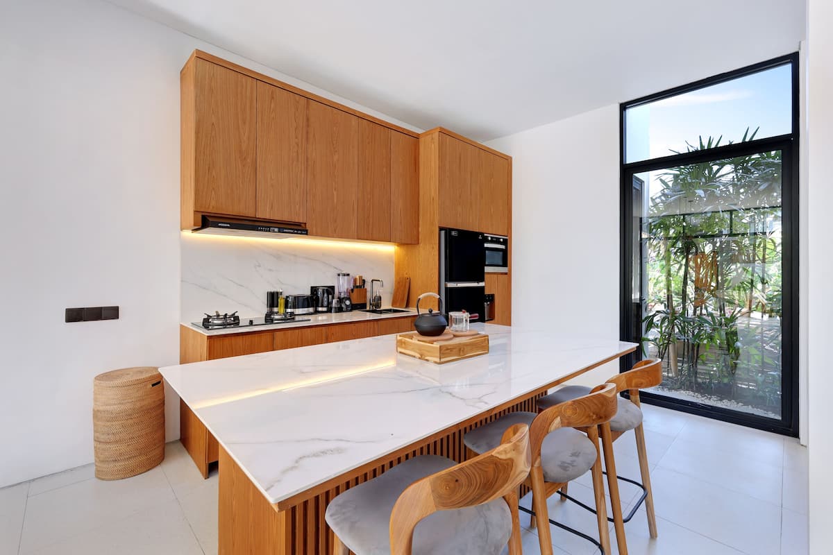 Una cocina moderna con armarios de madera, encimera de mármol y un amplio ventanal con vistas a zonas verdes.