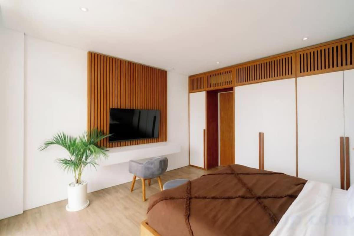 Un dormitorio moderno con cama, televisor montado en la pared, planta en maceta y puerta corredera.