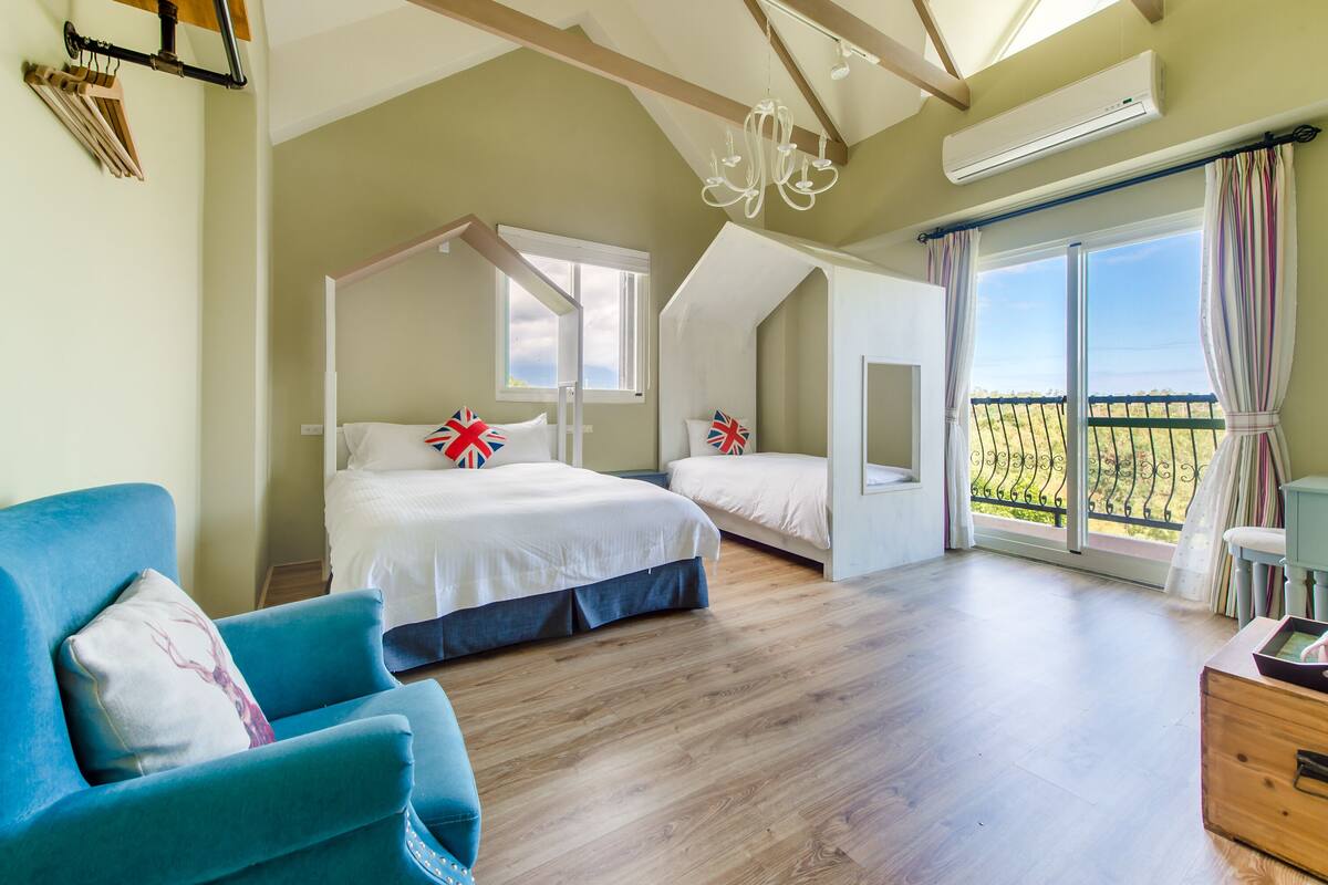 A bedroom with two beds, a large window, a balcony, and a chandelier.