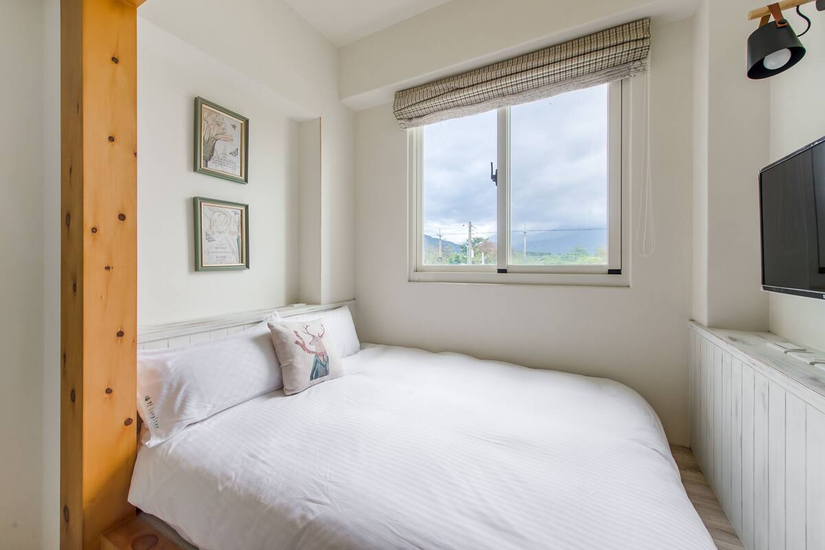 A bedroom with a bed, a window with a view, and a mounted TV.