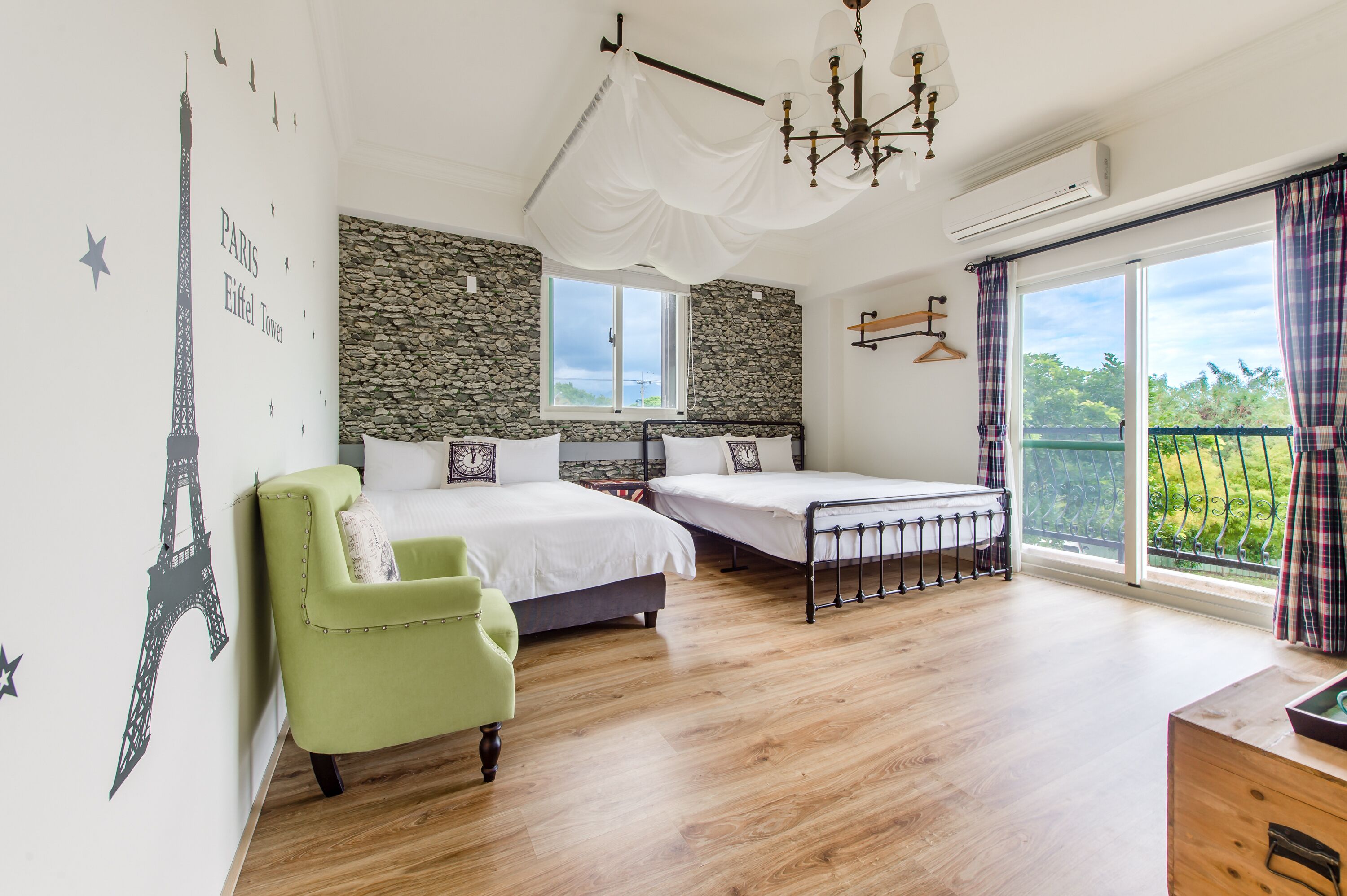 A bedroom with a stone wall, a bed, a chair, a balcony with curtains, and a view of greenery.