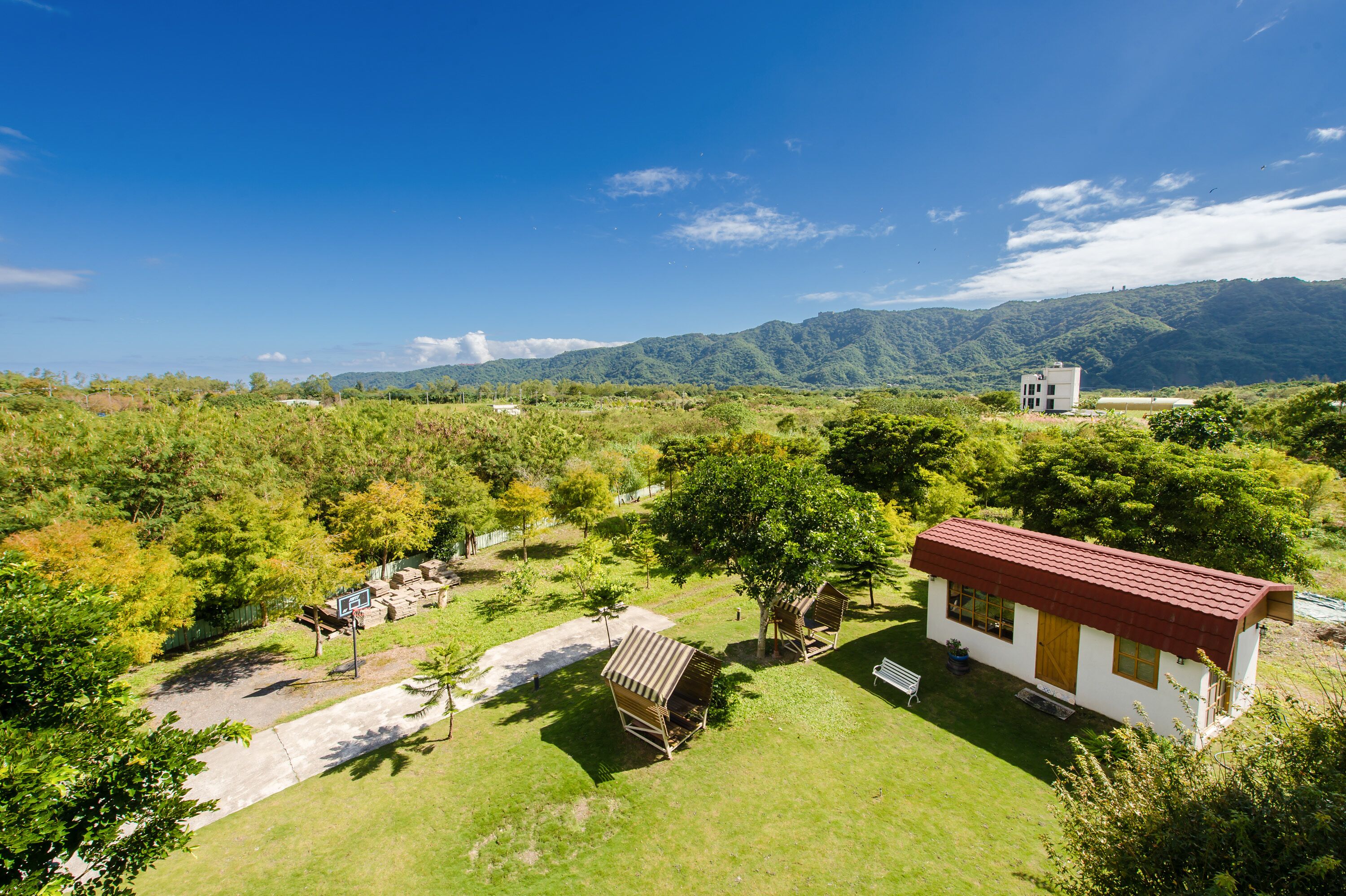 A small house with a red roof surrounded by lush greenery and a mountainous backdrop.