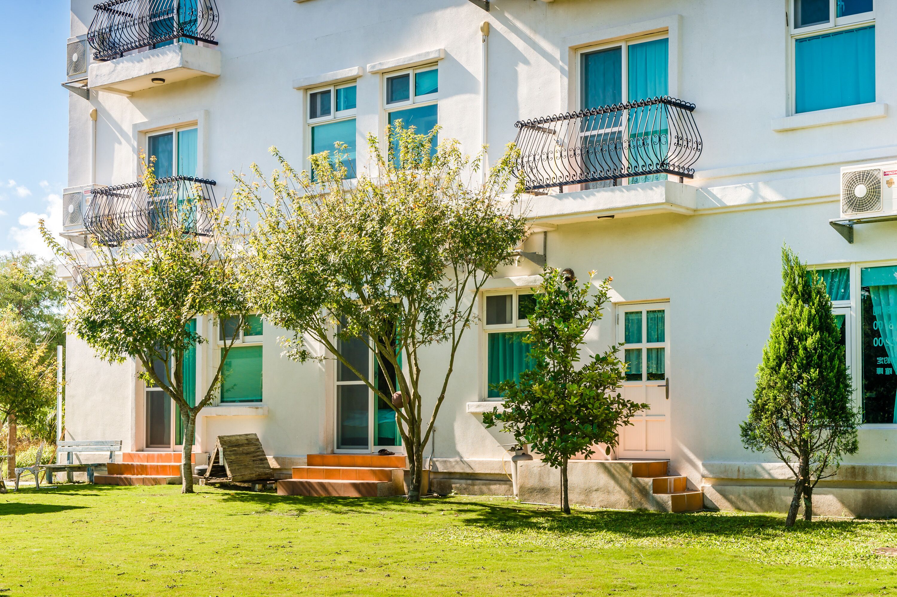 A multi-story building with balconies, a lawn, and a tree in front.