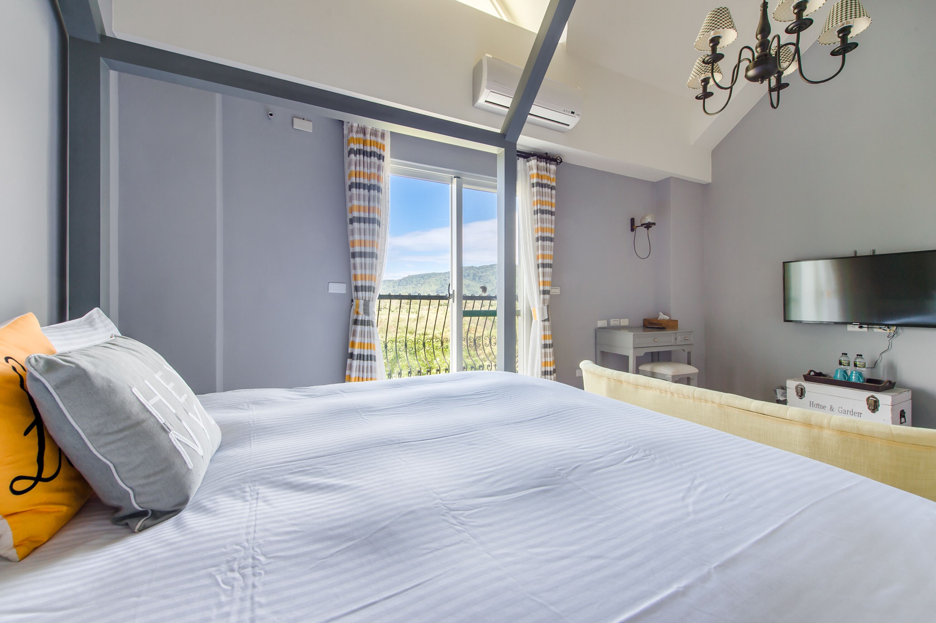 A hotel room with a large bed, a TV, a minibar, and a balcony with curtains.