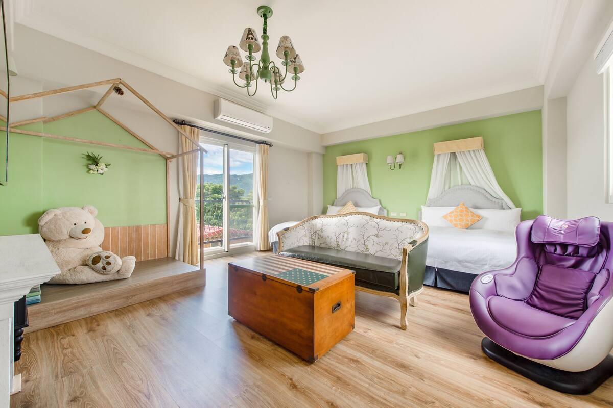 A room with a wooden floor, a sofa, a massage chair, a bed with a canopy, a teddy bear, and a wooden chest.