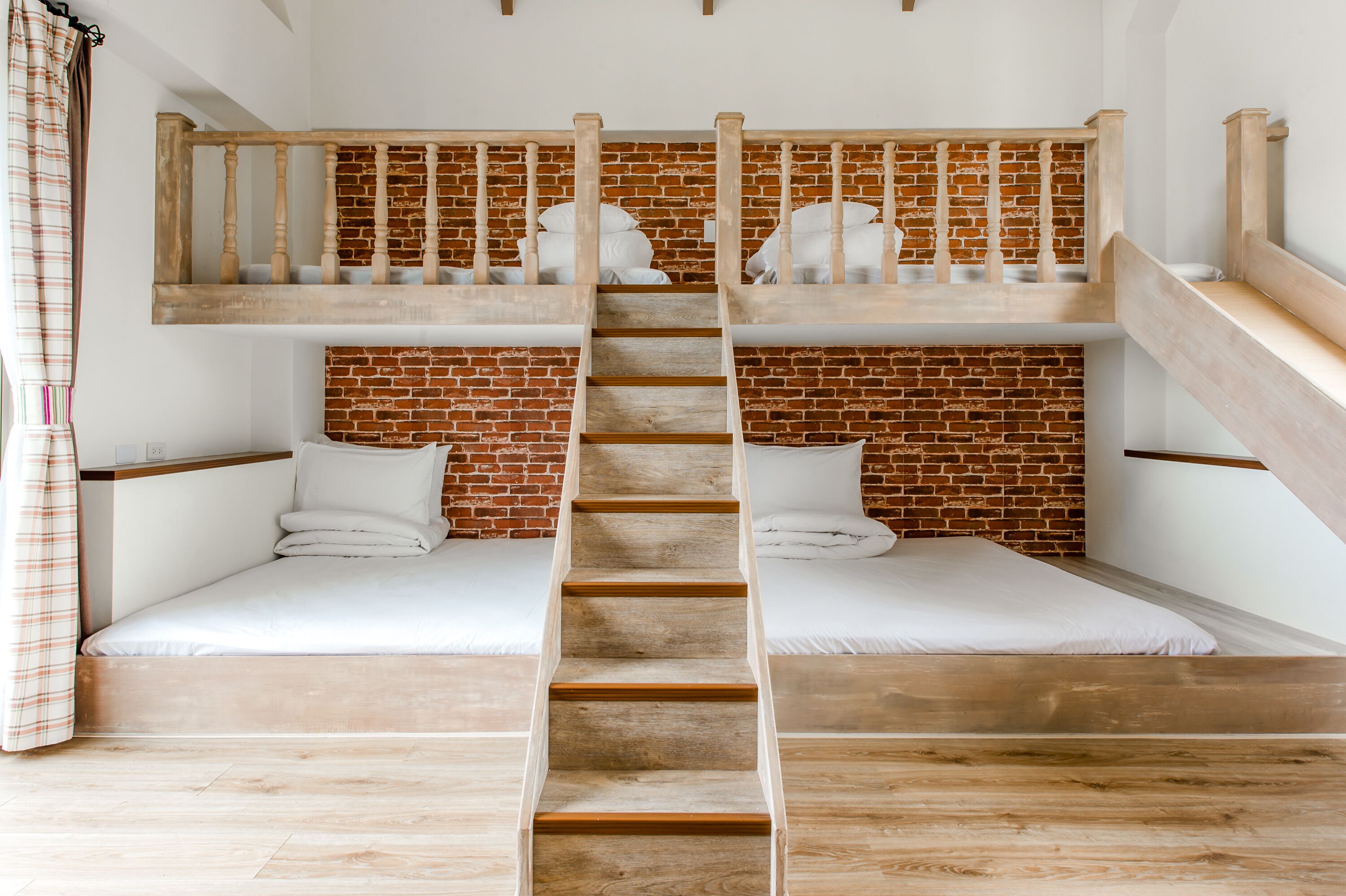 A bunk bed room with a wooden ladder, white bedding, and a brick wall.